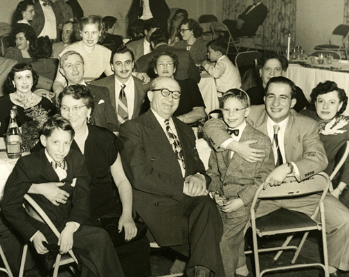Family wedding. 1950s. I’m on Henry’s lap. He was the sole survivor of his family after the war. We took him in to live with us. He later died, hit by a car crossing the street. Everyone thought it was survivor’s guilt. My brother Murray on left. In middle, grandparents, Morris and Esther. My mother in back, standing.